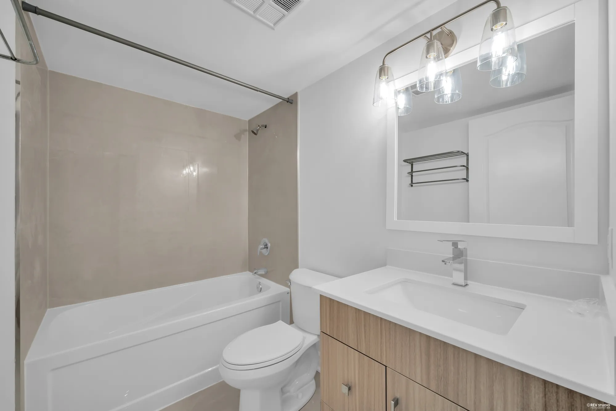 The bathroom: a tub with a tiled surround, a new vanity with a white counter, a wide mirror under a light bar