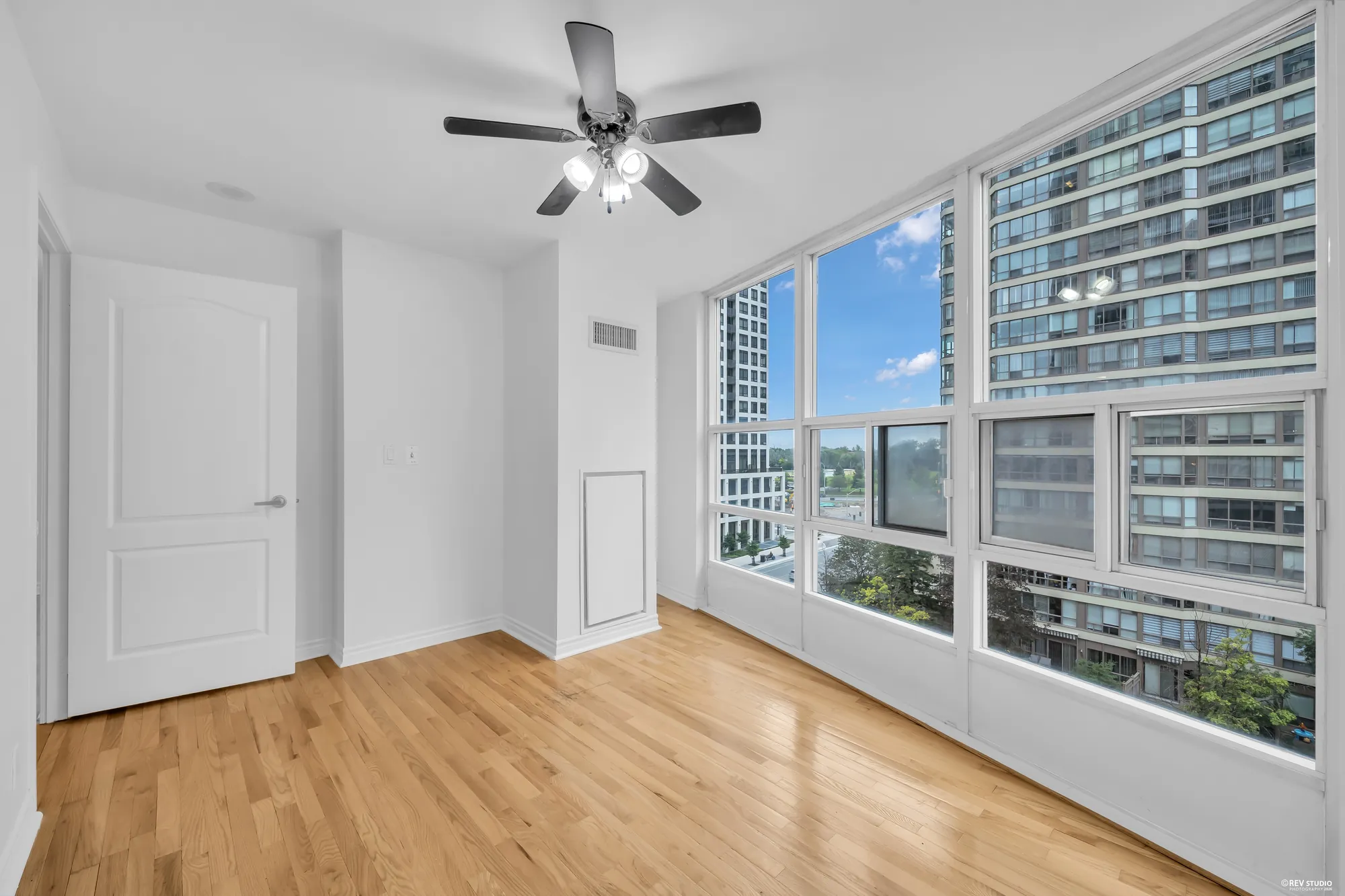 The bedroom's corner windows, empty: the towers across the courtyard, the door, hardwood