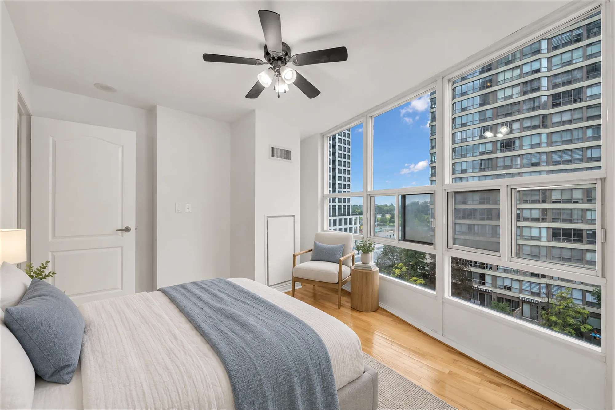 The same bedroom view virtually staged: a bed with a grey throw, a chair, a side table, a lamp and a rug