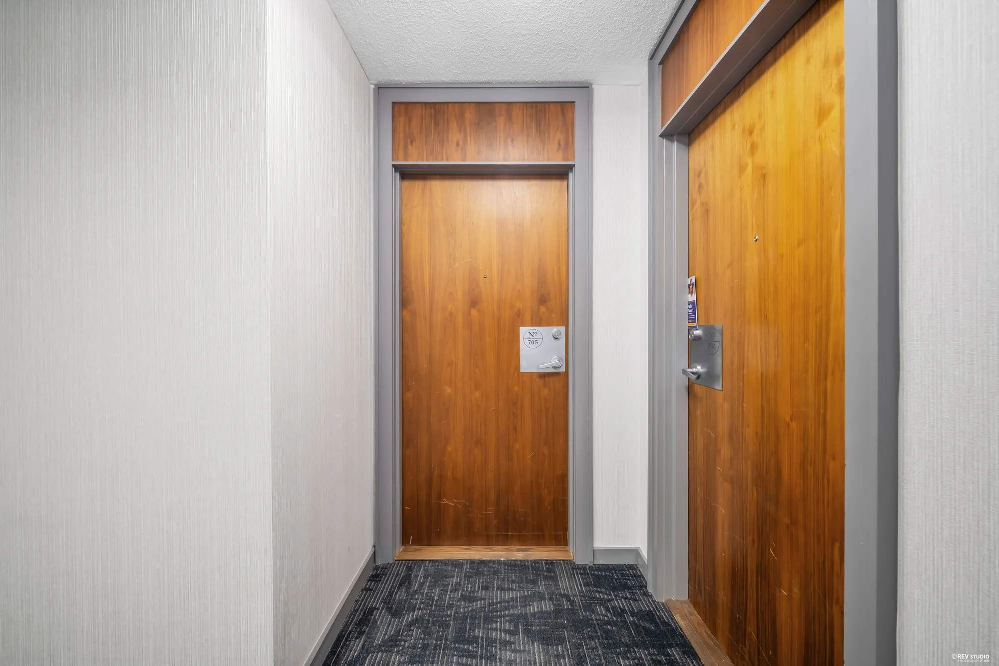 The apartment's wood door in the corridor, number 705, carpet and a light
