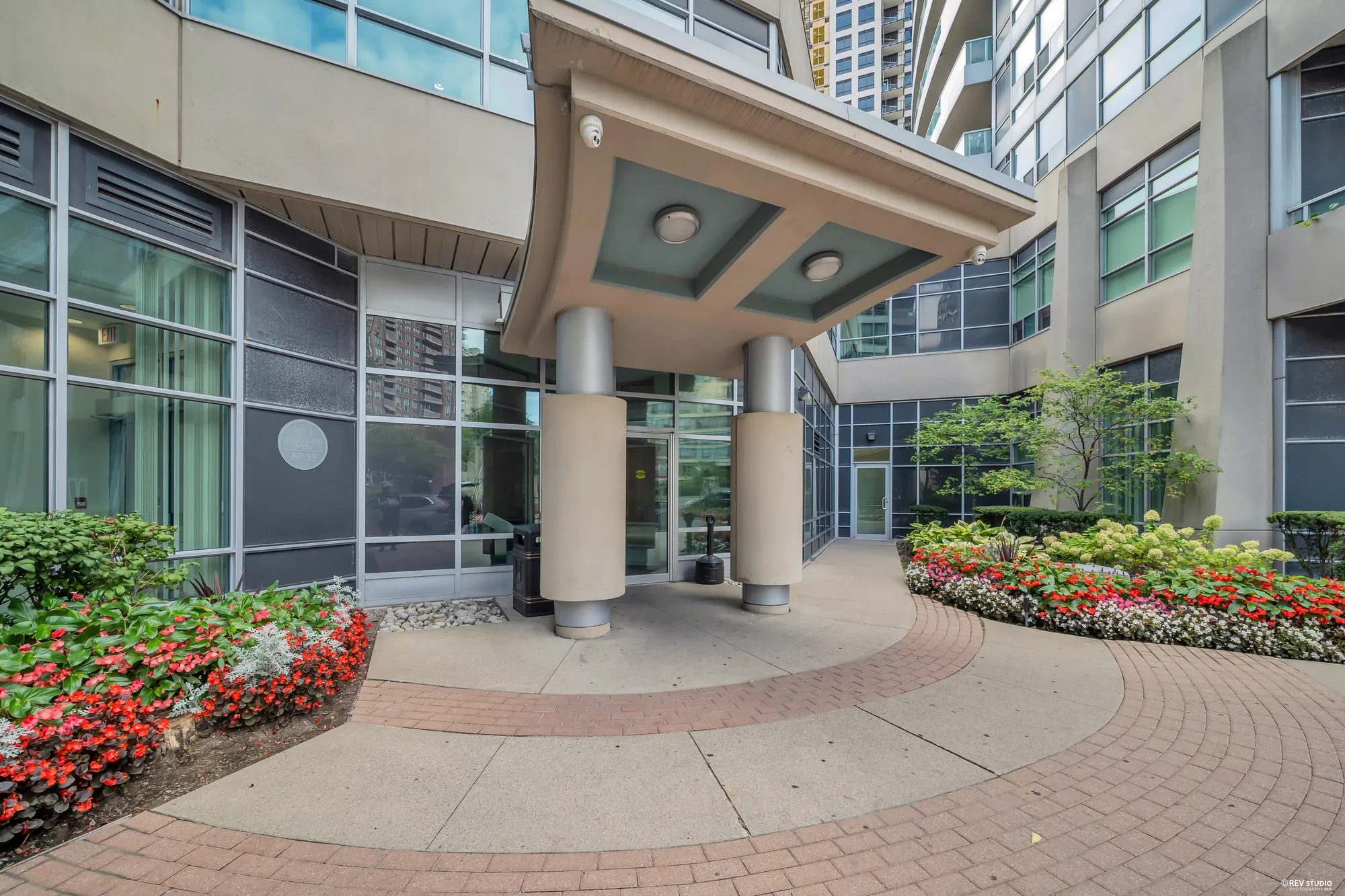 The entrance: a canopy on columns over a paved walk, flower beds either side, the tower above