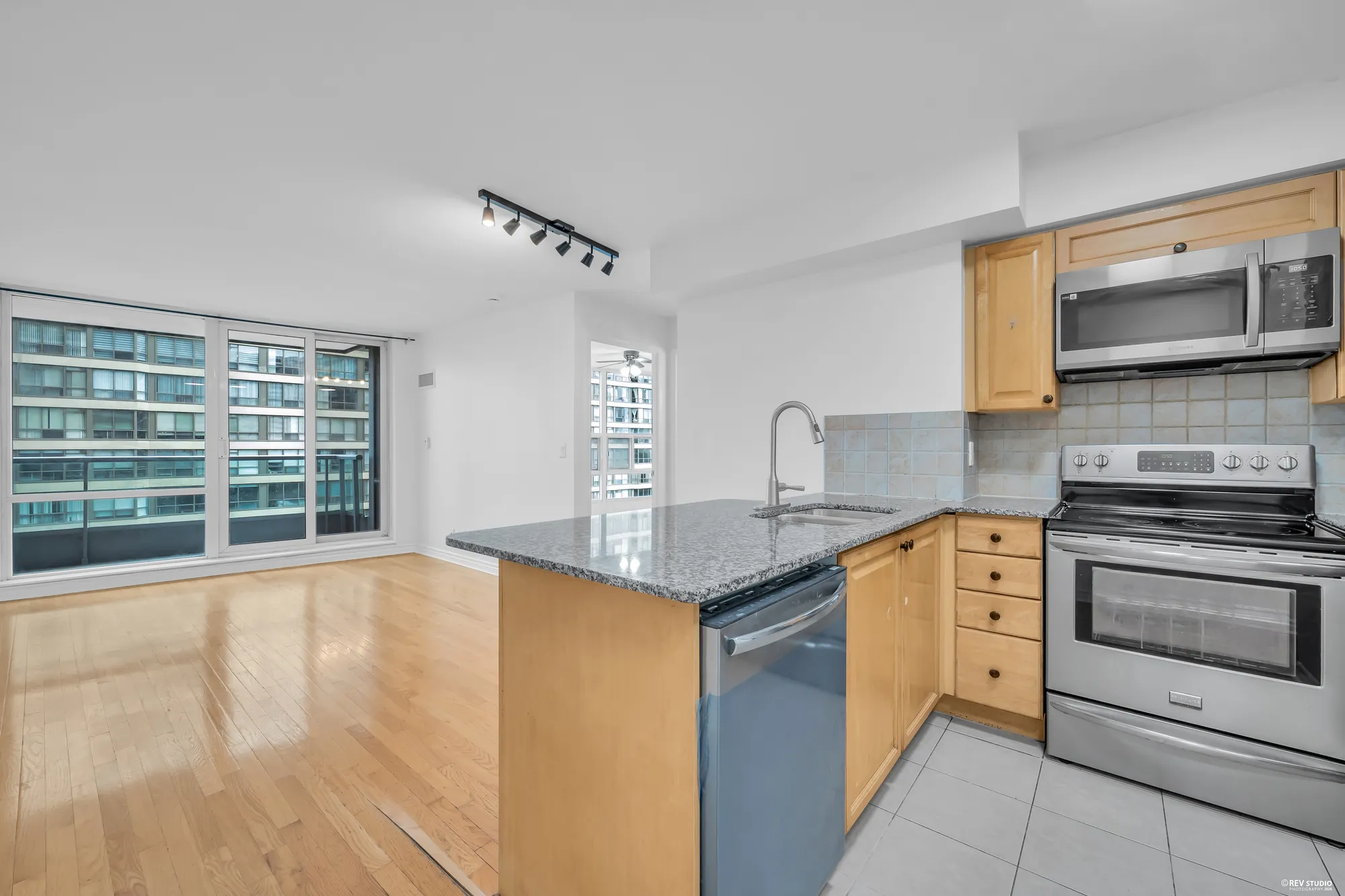 The kitchen: maple cabinets, granite counters, a stainless range with a microwave over it, the dishwasher, the peninsula, the living room and the glass beyond