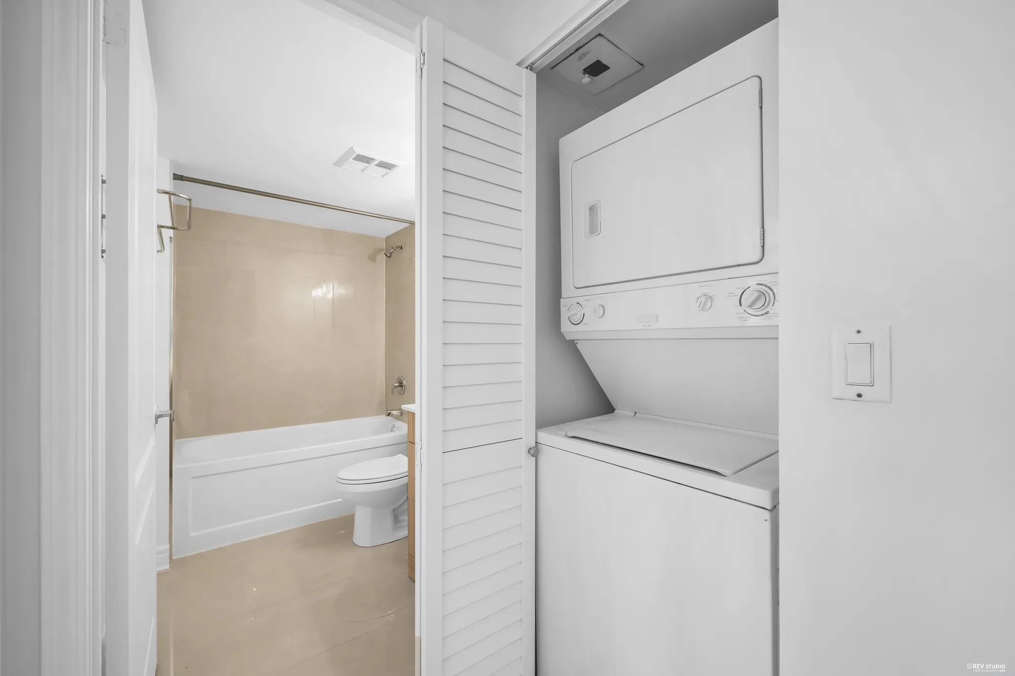 The laundry closet with a stacked washer and dryer, the bathroom door beside it