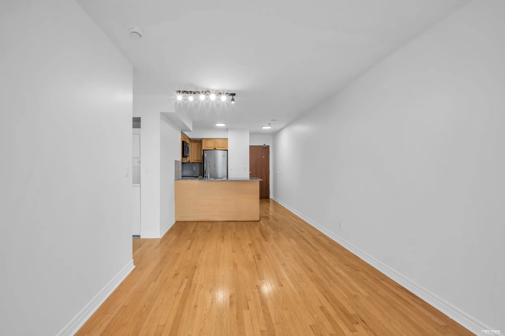 Down the length of the living room to the kitchen, empty: hardwood, the peninsula, the front door