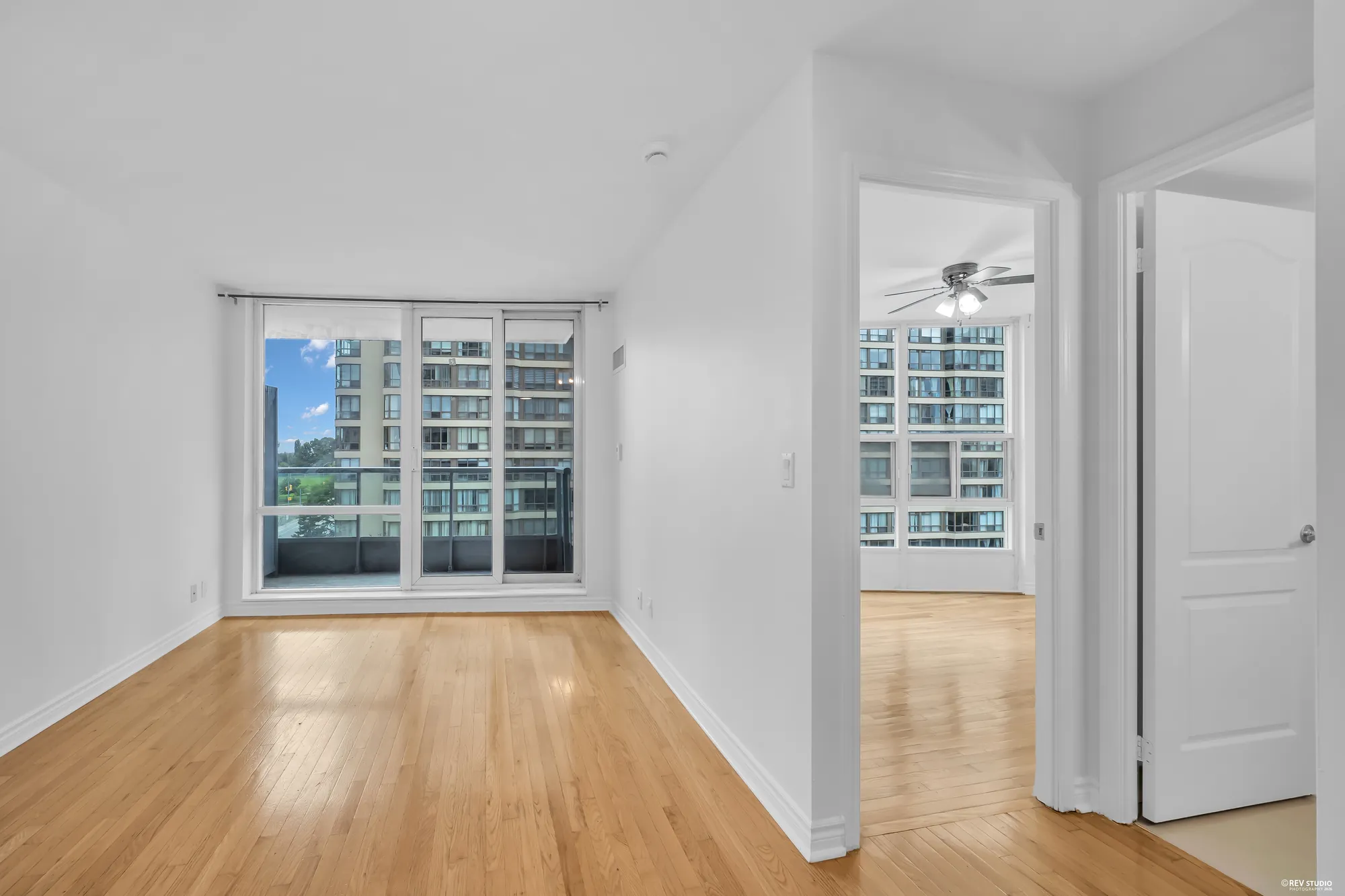 The living room toward the window wall and the bedroom door, the balcony beyond