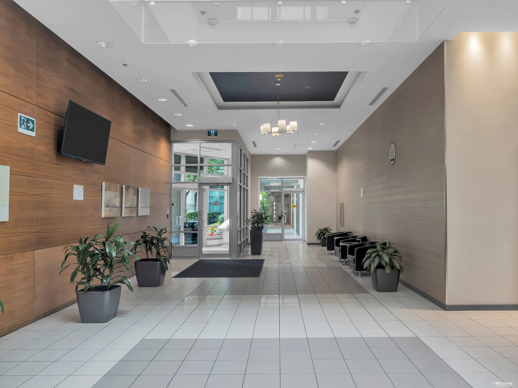 The lobby: a tiled floor, a wood-panelled wall with a screen, plants, a chandelier, the glass doors beyond