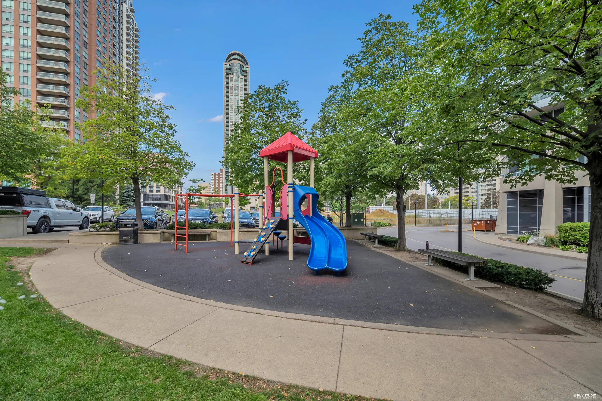 A playground with a red and blue slide under trees in the courtyard, the towers behind
