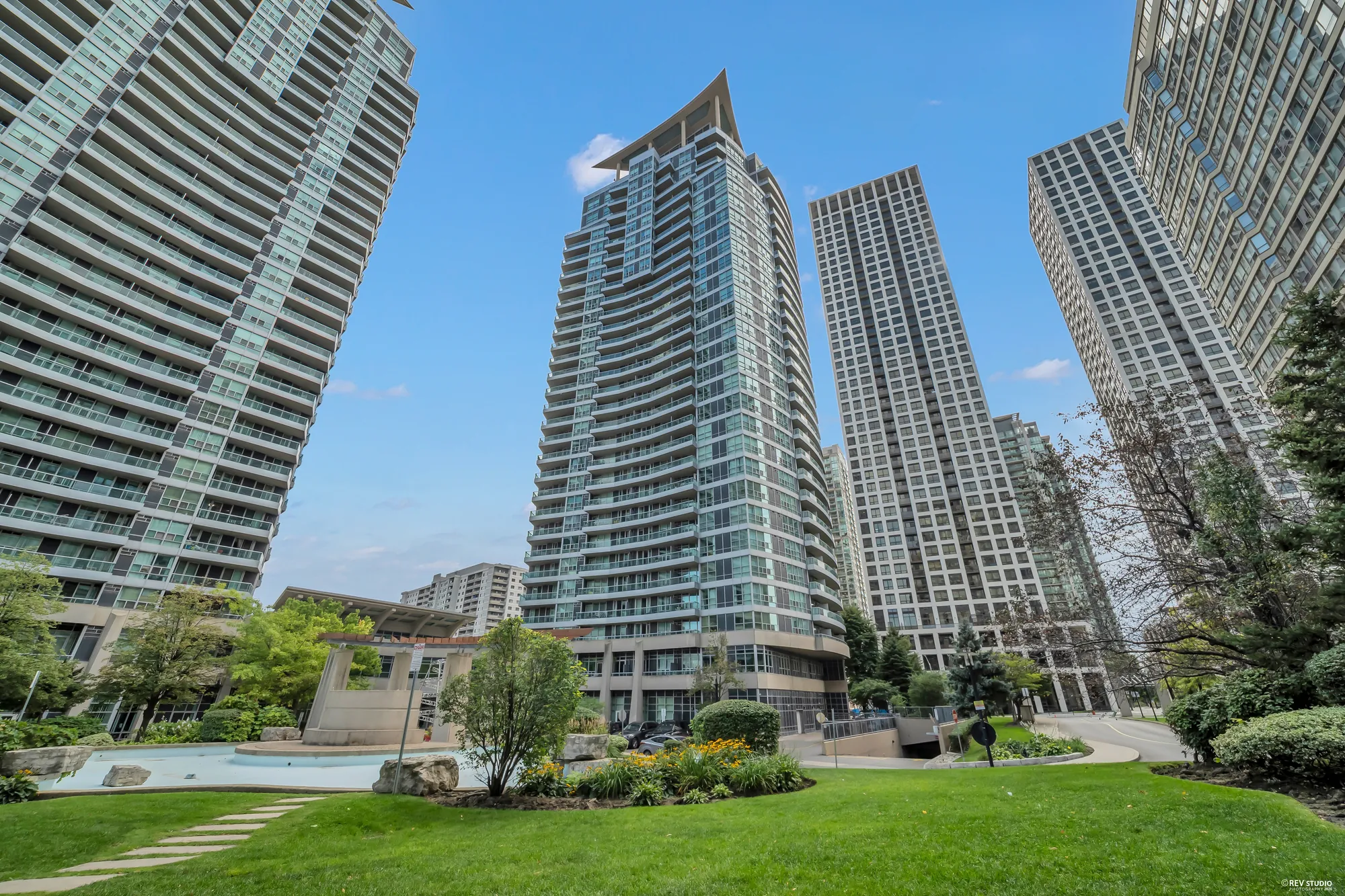 The towers of 33 Elm Drive West and its neighbours from the courtyard garden, glass and concrete against a blue sky